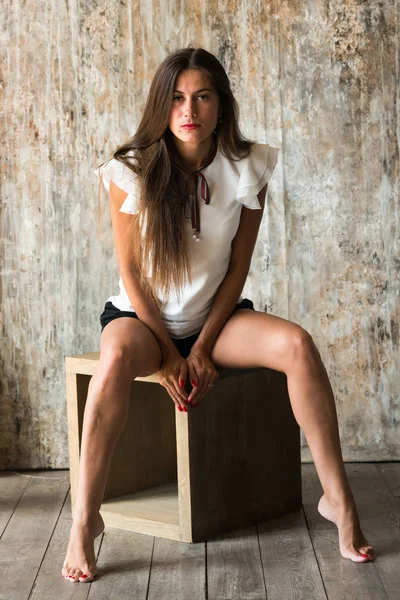 Concept portret van mooie mooie brunette meisje op grijze achtergrond in Studio zittend op kubus voor camera. — Stockfoto