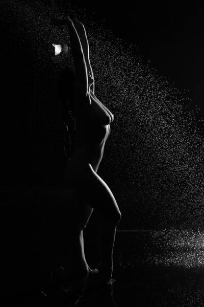 Sexy woman in shower. Attractive young naked woman under water drops on black background.