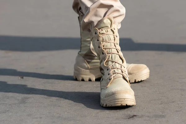Light military shoes on the feet on the background of asphalt