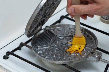 Fırçalama kabını fırçala. Waffle yapmak için yağ formuyla lekelemek. Waffle pişiriyorum. Cihazı evde gaz sobasında tatlı yapmak için yağlayın