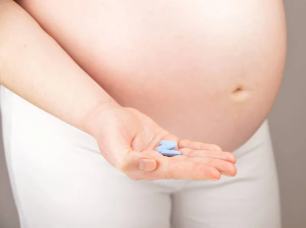 A cropped shot of a pregnant woman with a pill in his hand against a white background and self-medication