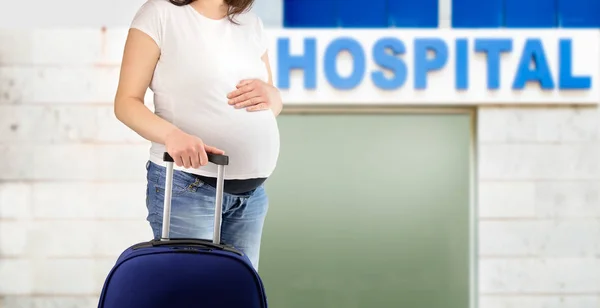 スーツケース次病院建物と待っている妊娠中の女性 — ストック写真