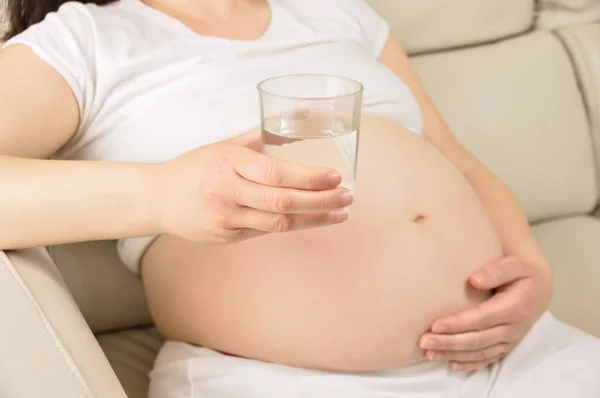 Kobieta Ciąży Siedzi Sali Żywo Myślenia Trzymając Szklankę Wody — Zdjęcie stockowe