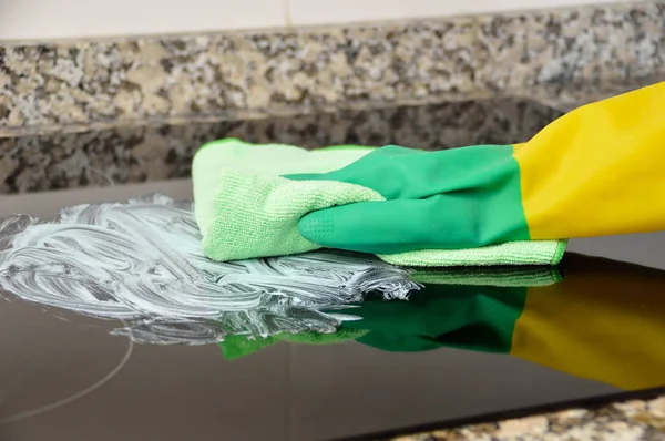一个被辨认的人用黄色和绿色手套在厨房擦洗烤箱的表面的射击 — 图库照片
