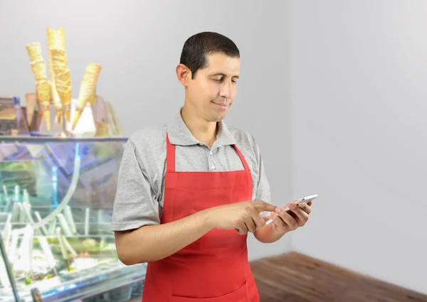 Smiling ice cream store employee standing behind the counter in the store and uses a phone