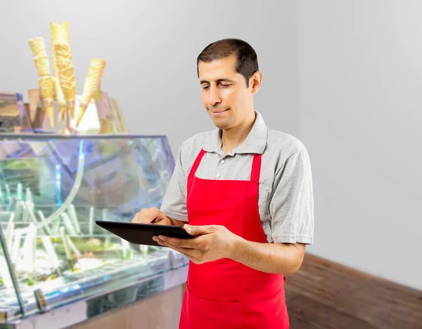 Smiling ice cream store employee standing behind the counter in the store and uses a digital tablet