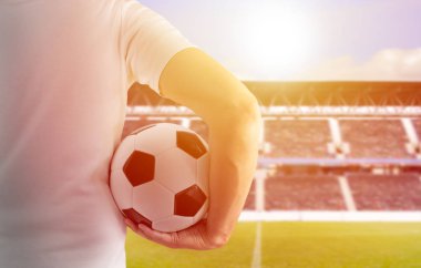 Kırpılan dikiz görüntü arka plan gün batımı ile Madrid Stadyumu'nda bir futbol topu onun silah altında tutan bir genç oyuncu adamın