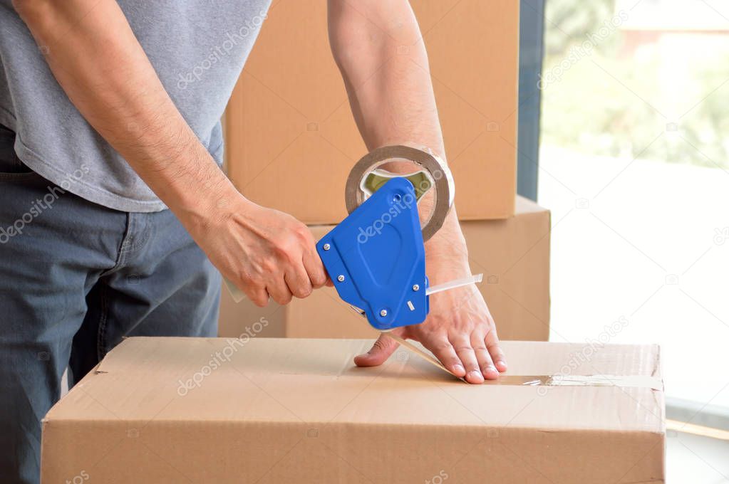 Shot of an unidentifiable young man closing a cardboard box with tape at home