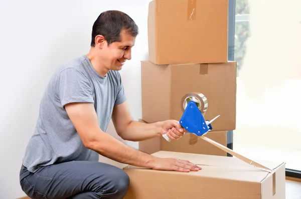 Shot of an man closing a cardboard box with tape at home