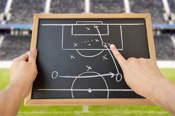 hand of a football coach drawing a tactics of soccer game with white chalk on blackboard at stadium background