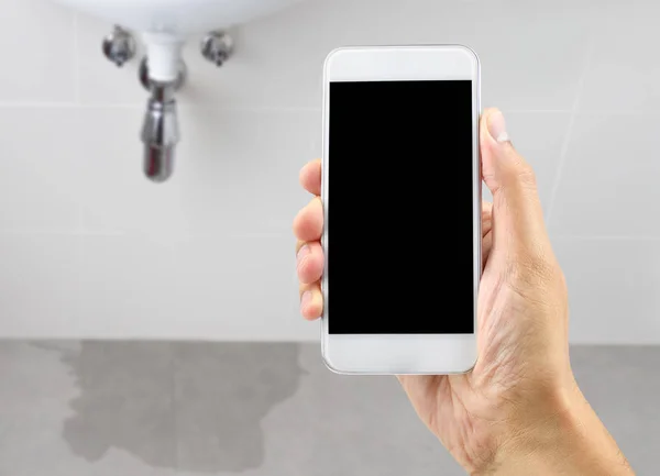 A hand holding a smartphone to call the professional to repair a water leak in the bathroom