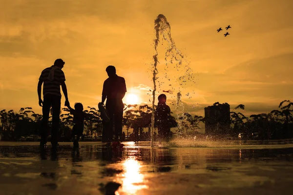 日落时在喷泉中玩耍的家庭剪影 — 图库照片