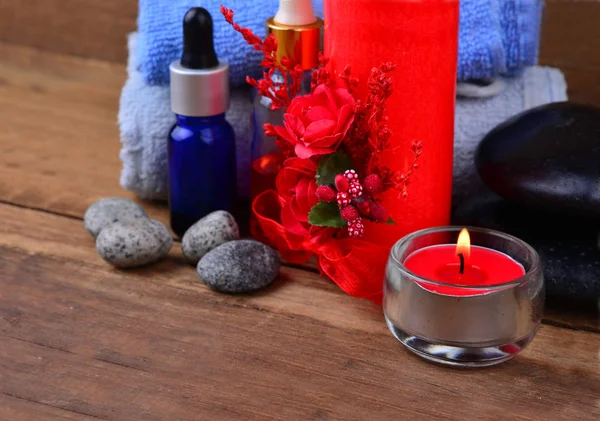 Red romantic candle and spa oil with towel and zen stone on wooden table