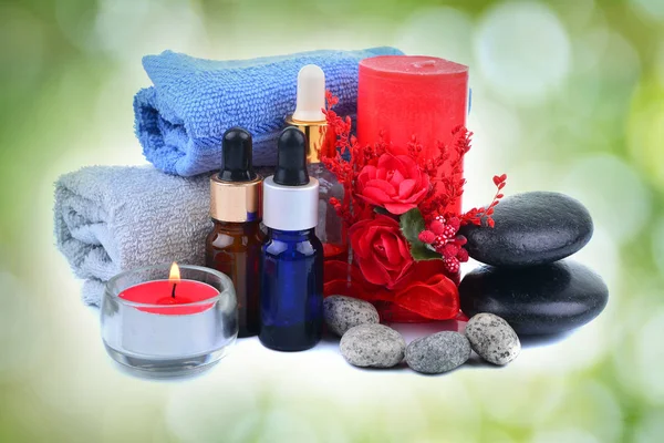 Red romantic candle and spa oil with towel and zen stone over green blur bokeh background