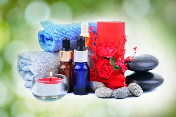 Red romantic candle and spa oil with towel and zen stone over green blur bokeh background