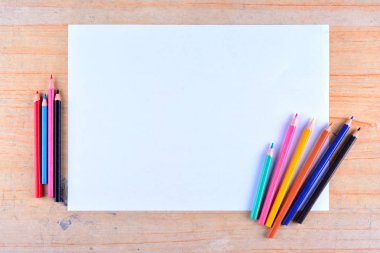 Boş kağıt ve ahşap masada renkli kalemler. Yukarıdan görüntüle