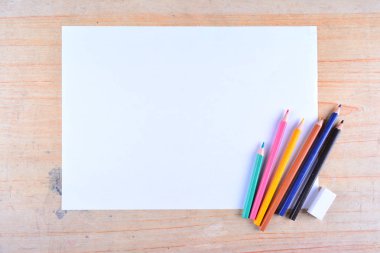 Boş kağıt ve ahşap masada renkli kalemler. Yukarıdan görüntüle