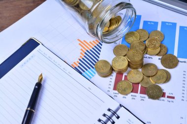 sikkeler, kavanoz, defter, çizelgeler ve masadaki kalem