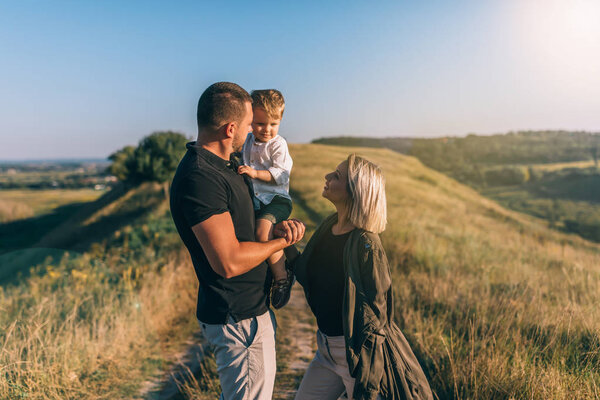 happy young parents looking at adorable little son while standing on rural path 