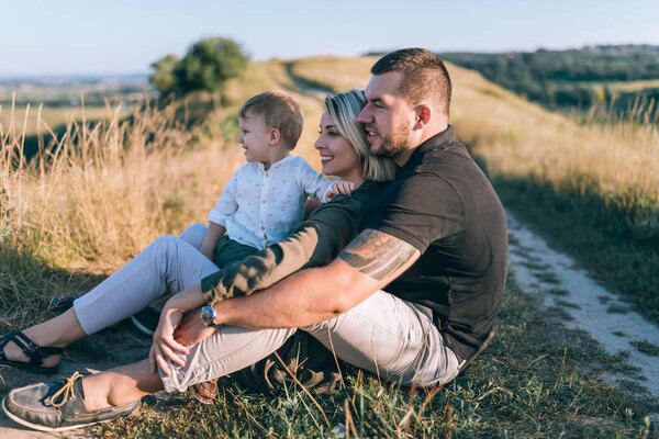 happy parents with adorable little son sitting and looking away in rural landscape