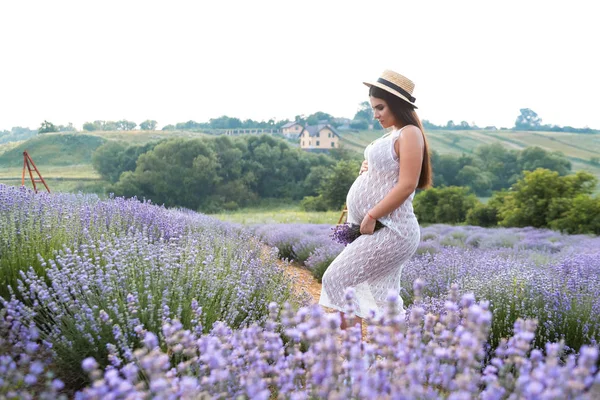 Side view of pregnant woman touching belly and holding lavender flowers — Stock Photo