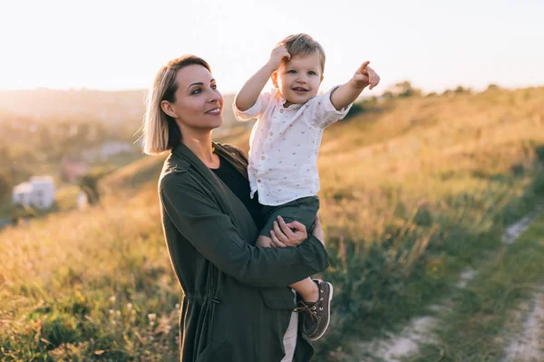 Feliz joven madre llevando adorable pequeño hijo señalando con el dedo al aire libre - foto de stock