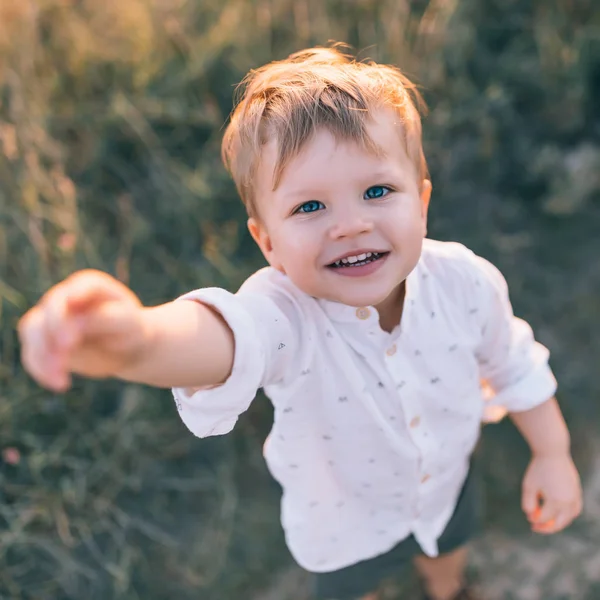 Vista ad alto angolo di adorabile bambino felice che raggiunge la mano e sorride alla fotocamera all'aperto — Foto stock
