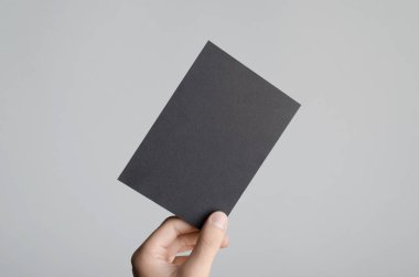 Siyah A6 Flyer / Kartpostal / Davetiye Model-up - Gri arkaplanda siyah bir el ilanı tutan erkek eller.