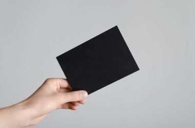 Siyah A6 Flyer / Kartpostal / Davetiye Model-up - Gri arkaplanda siyah bir el ilanı tutan erkek eller.