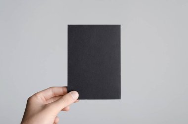 Siyah A6 Flyer / Kartpostal / Davetiye Model-up - Gri arkaplanda siyah bir el ilanı tutan erkek eller.