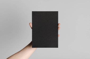 Siyah A5 broşürü / davet Mock-Up - erkek eller gri bir arka plan üzerinde siyah bir el ilanı holding.