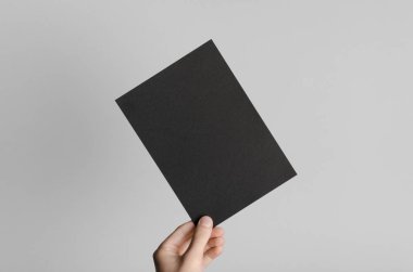 Siyah A5 broşürü / davet Mock-Up - erkek eller gri bir arka plan üzerinde siyah bir el ilanı holding.