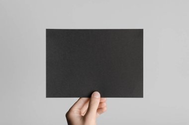 Siyah A5 broşürü / davet Mock-Up - erkek eller gri bir arka plan üzerinde siyah bir el ilanı holding.