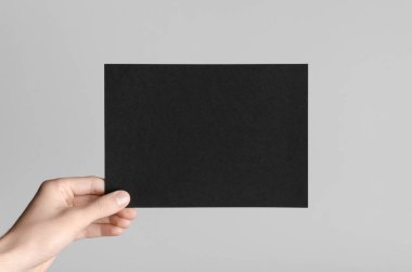 Siyah A5 broşürü / davet Mock-Up - erkek eller gri bir arka plan üzerinde siyah bir el ilanı holding.