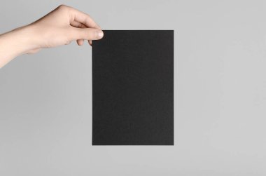 Siyah A5 broşürü / davet Mock-Up - erkek eller gri bir arka plan üzerinde siyah bir el ilanı holding.