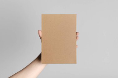 Kraft A5 broşürü / davet Mock-Up - kraft el ilanı gri bir arka plan üzerinde tutan eller erkek.