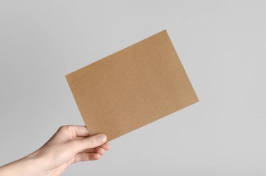 Kraft A5 broşürü / davet Mock-Up - kraft el ilanı gri bir arka plan üzerinde tutan eller erkek.