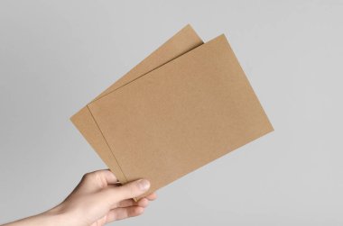 Kraft A5 broşürü / davet Mock-Up-kraft el ilanları gri bir arka plan üzerinde holding erkek eller.