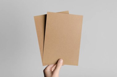 Kraft A5 broşürü / davet Mock-Up-kraft el ilanları gri bir arka plan üzerinde holding erkek eller.