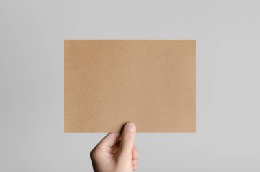 Kraft A5 broşürü / davet Mock-Up - kraft el ilanı gri bir arka plan üzerinde tutan eller erkek.