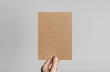 Kraft A5 broşürü / davet Mock-Up - kraft el ilanı gri bir arka plan üzerinde tutan eller erkek.