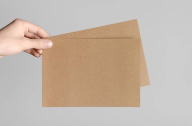 Kraft A5 broşürü / davet Mock-Up-kraft el ilanları gri bir arka plan üzerinde holding erkek eller.