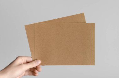 Kraft A5 broşürü / davet Mock-Up-kraft el ilanları gri bir arka plan üzerinde holding erkek eller.
