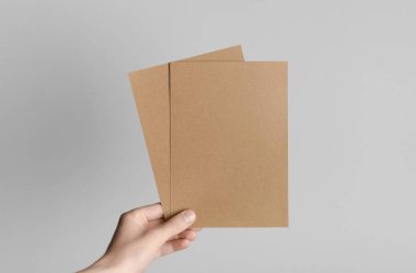 Kraft A5 broşürü / davet Mock-Up-kraft el ilanları gri bir arka plan üzerinde holding erkek eller.