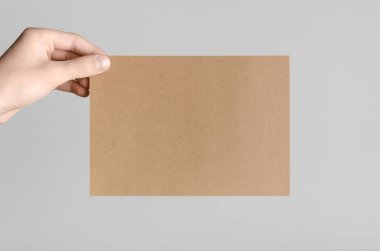 Kraft A5 broşürü / davet Mock-Up - kraft el ilanı gri bir arka plan üzerinde tutan eller erkek.
