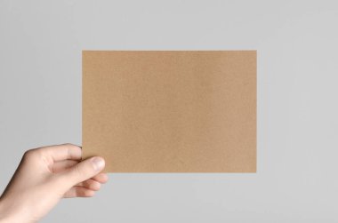 Kraft A5 broşürü / davet Mock-Up - kraft el ilanı gri bir arka plan üzerinde tutan eller erkek.