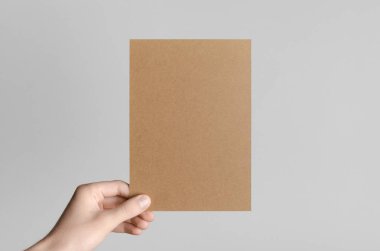 Kraft A5 broşürü / davet Mock-Up - kraft el ilanı gri bir arka plan üzerinde tutan eller erkek.