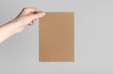 Kraft A5 broşürü / davet Mock-Up - kraft el ilanı gri bir arka plan üzerinde tutan eller erkek.