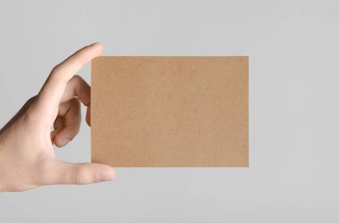 Kraft A6 el ilanı / kart / davet Mock-Up - kraft el ilanı gri bir arka plan üzerinde tutan eller erkek.