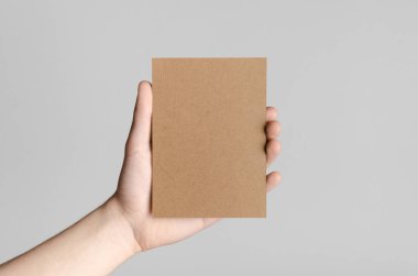 Kraft A6 el ilanı / kart / davet Mock-Up - kraft el ilanı gri bir arka plan üzerinde tutan eller erkek.